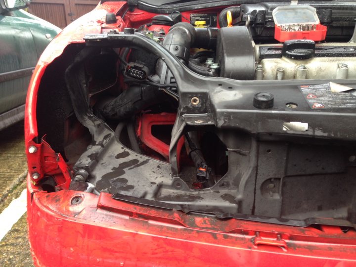 Lupo bodywork repair advice - Page 1 - Home Mechanics - PistonHeads - The image showcases the underside of a red car, which appears to be a Honda CRV, in the midst of a service or car wash. The engine bay door is missing, exposing parts of the engine and transmission. The car is parked on an asphalt surface, and the surrounding area suggests it might be a workshop or a dedicated space for car washing. There's a visible water spray, which indicates the car is in the process of being washed. The hood is bent open, and several tools are scattered around the engine area, suggesting ongoing work or a just-completed thorough cleaning.