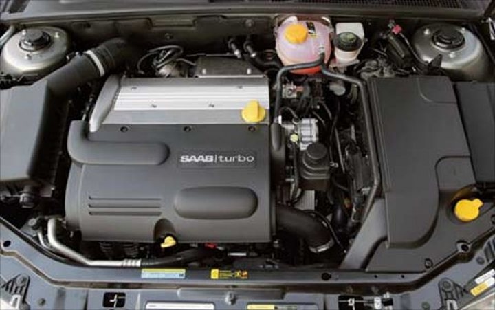 Does my 93 have a GM engine? - Page 1 - Saab - PistonHeads - The image shows the engine bay of a car, with the hood open. The engine is prominently displaying the Volkswagen logo, identifying it as a turbocharged SAAB unit. There are visible fuel lines and connections beneath the engine, and several stickers and tags are attached to various components, possibly for maintenance or safety purposes. Additionally, there are signal horns on the car's roof, which are part of emergency signaling systems. The interior of the car has yellow caps to cover various systems.