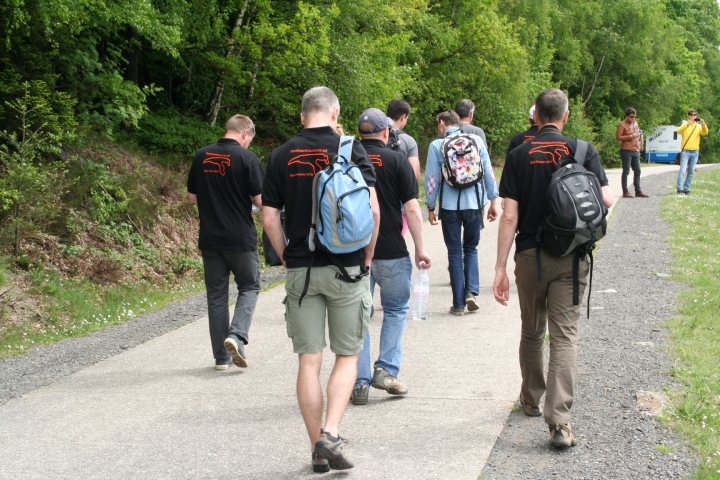 A group of people walking down a street - Pistonheads - In the image, a group of young people is walking down a dirt path. They are all dressed casually, with backpacks on their backs indicating they might be on a hike or a day trip. The path they are on is bordered by lush green trees and bushes, suggesting it could be a trail through a forest or a park. The terrain looks rocky in some areas, typical for a hiking trail. There are no visible buildings or structures in the immediate vicinity, and the focus of the image is clearly on the group of outdoor enthusiasts.