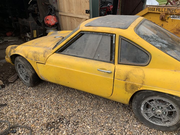 Classics left to die/rotting pics - Vol 2 - Page 340 - Classic Cars and Yesterday's Heroes - PistonHeads UK - The image showcases a rusted, yellow sports car parked in what appears to be a garage or workshop. The car is covered in dust and dirt, suggesting it has not been used for some time. A person can be seen in the background, but they are partially obscured by a door and do not seem to interact with the car. The setting indicates that this vehicle may have been stored or abandoned for quite some time.