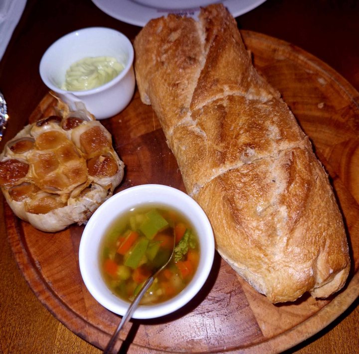 Pistonheads - The image captures a delightful meal scene. On the right side of the frame, there's a long loaf of bread that has been sliced and arranged neatly on a wooden cutting board. Accompanying the bread, there's a small bowl filled with dipping sauce, likely oil or vinegar, placed next to it. 

The cutting board is set against a dark background, which contrasts nicely with the light-colored bread and bowl. In the foreground, on the left side of the image, there's a spoon resting inside a small bowl filled with a green sauce. The spoon appears to be ready for serving or dipping, suggesting that it's time to enjoy this meal.

The overall setting seems to be a casual dining environment, perhaps in a home or a restaurant. The wooden table and the presence of a spoon suggest that the meal is about to begin. The image exudes a warm and inviting atmosphere, making one anticipate the flavors and textures of this delicious spread.