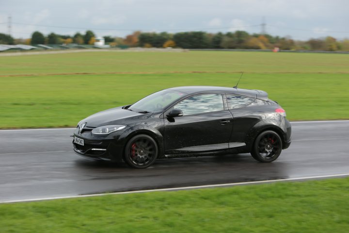 Cars that you keep going back to - Page 4 - General Gassing - PistonHeads - The image captures a dynamic scene on a racetrack. Dominating the center of the frame is a black SUV, captured in motion as it races along the track. The car's speed has resulted in a vibrant blur behind it, emphasizing its swift pace.

The track itself appears to be wet, hinting at recent rainfall. A scattering of trees can be seen in the background, adding a touch of nature to this high-octane setting.

On the right side of the image, there's a person visible, possibly a track worker or marshal, observing the car's progress. Their presence adds a human element to the scene, reminding us that this is not just an empty circuit, but a place where racing takes place.