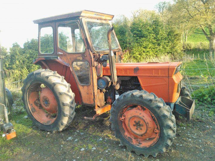 Classic tractors - Page 5 - Classic Cars and Yesterday's Heroes - PistonHeads - The image showcases a small, old tractor standing in an outdoor setting, likely a farm. The tractor, exhibiting signs of wear and age, is predominantly orange and black in color. Its stationary position in what appears to be a field suggests it is not currently in use. The background hints at an agricultural or pastoral environment, possibly indicating a countryside or rural location. The tractor does not seem to be in motion, and there are no indications of people or other vehicles in the immediate vicinity, implying a quiet and perhaps historical moment captured in the image.