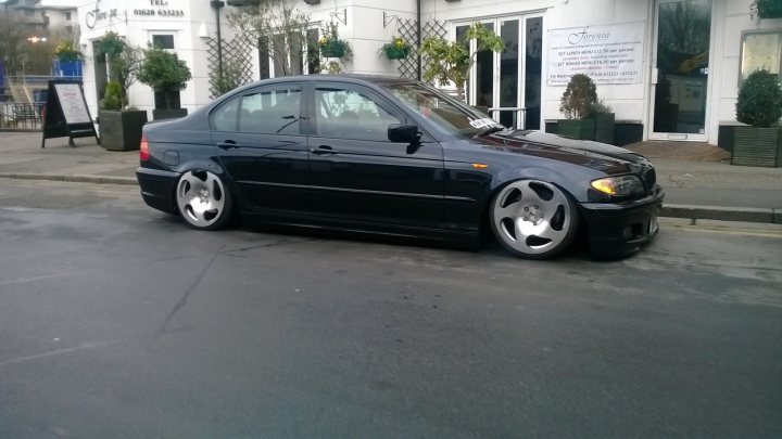 A car parked on the side of the road - Pistonheads - The image showcases a blue B6 BMW parked on the street. The car is positioned facing the sidewalk with the BMW logo prominently visible on the front grill. The pavement is wet, reflecting the car's body and gleaming in the daylight. 

In the background, there's a white building adorned with green plants and shrubbery on the facade. The building seems to have curtains allowing a glimpse of the indoor setting. A couple of potted plants are also part of the decoration outside the building, with one positioned near the car on the sidewalk. 

The overall scene suggests a peaceful urban environment where the BMW car adds a touch of elegance to the neighborhood.