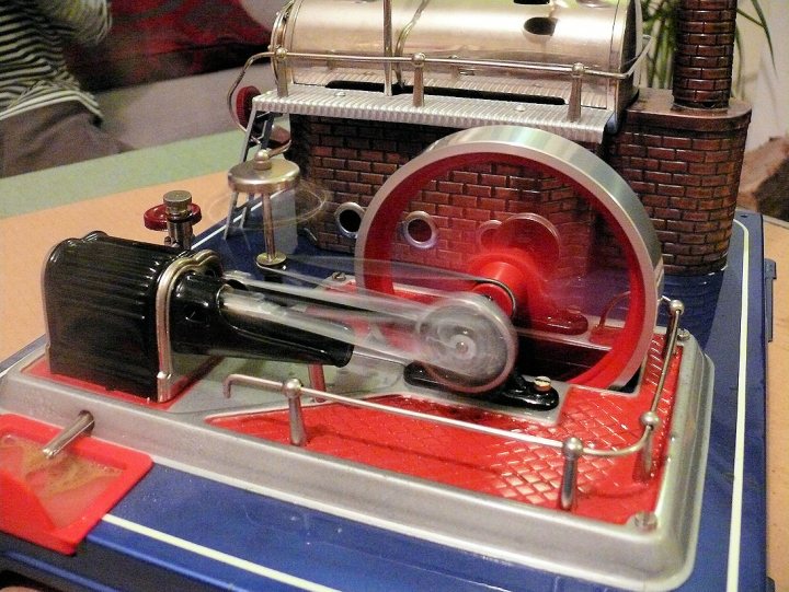 An old fashioned stove in a small kitchen - Pistonheads - The image shows a small, detailed diorama. At the center is a model of a toy train engine. The train engine is red and black, with visible wheels and a smoke stack. Connected to the front of the engine is a black, cylindrical rod labeled "Taiyal" and a clear glass part labeled "Rotors." Above the train engine, there is a structure resembling a chimney or tower, which likely represents a smoke stack or similar feature. The surrounding diorama features what appears to be a track to the left and a blue base, possibly a platform or baseplate, beneath the train model. The overall scene is meticulously crafted and looks like a model railroad setting, designed to give a realistic representation of the train.