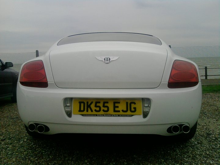 Continental Bentley Pistonheads - The image features a white subcompact car on what seems to be a gravel or gravel-like surface. The car is branded with the manufacturer's logo, which resembles a circular wing symbol, prominently displayed on the trunk. The license plate reads "DK55 EJG." The background is somewhat blurry, but it appears to be an outdoor lot with sky and trees visible in the distance, suggesting a partly cloudy day. The lighting conditions suggest the photo might have been taken either in the morning or late afternoon.