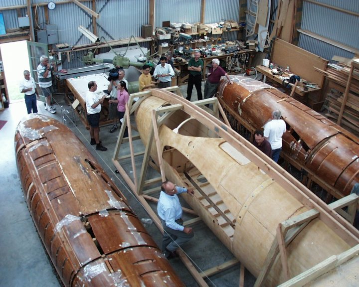 Post amazingly cool pictures of aircraft (Volume 2) - Page 415 - Boats, Planes & Trains - PistonHeads - The image captures a bustling scene inside a workshop or warehouse. A group of people are engrossed in examining and working on wooden boats that are lined up along the walls. There are four boats in total, all with rich, brown wood, each in various stages of assembly or repair. The room is well-lit by fluorescent lights, casting a bright glow on the wooden planks of the boats and the tools scattered around the workspace. In the background, there's a person standing near a workbench, possibly supervising the work being done. A sign reading "30 days" can be spotted, indicating perhaps the deadline for this project or a countdown timer for some ongoing process.