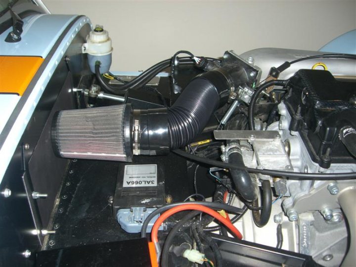 Duratec Heater Delete Pistonheads - The image displays the open hood of an automobile, with various components visible. At the center, a black foam air filter housing can be seen, situated near the engine bay. Surrounding the main engine is a network of wires and cables, which appear to be colored red, and possibly black, indicating different circuits or systems. The engine parts are metallic and have various shapes and sizes. The background is dimly lit, suggesting an indoor or garage setting, which is typical for automotive repairs and maintenance. The overall condition of the area suggests it is undergoing some mechanical work or diagnostic testing. No significant brand markings or specific model indicators are immediately apparent from this angle.