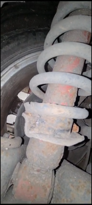 Pistonheads - The image shows a close-up of a rusty coil spring, which appears to be part of a vehicle's suspension system. The spring is encased in a worn out bracket with visible signs of rust and wear. The background suggests that the part is located near the tire area of the vehicle. The image generally displays a mechanical component in a state of disrepair, highlighting the maintenance needed for vehicles.