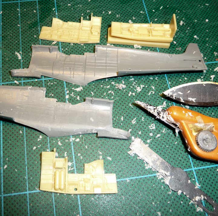 Tamiya 1:72 Spitfire Mk1 + Details - Page 1 - Scale Models - PistonHeads - The image shows a workbench filled with model building materials. There are numerous pieces of plastic figurines, each varying in size and shape, scattered across the green surface of the table. Among the model parts, there are tools present, such as a pair of scissors, a box cutter, and possibly a hobby knife and a small drill bit. The layout suggests an active work session, perhaps of a hobbyist or a toy enthusiast. The scene captures the essence of a crafting project or a detailed assembly of a small model.