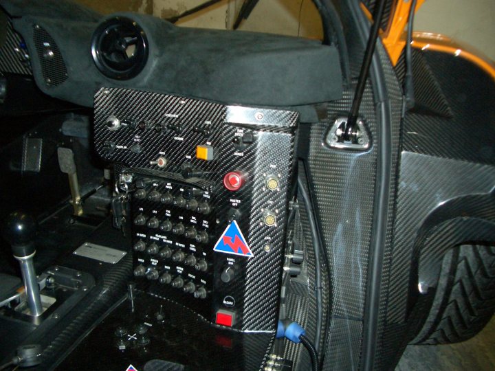 £3.5million for a Mac F1 - Page 7 - Supercar General - PistonHeads - The image shows a close-up of the dashboard and control panel of a vehicle. The panel appears to be a complex array of switches and buttons, with a circular label partitioned into four sections and labeled "COMPRESSOR", "LIGHTS", "AIR", and "STARTER". The dashboard is black with a carbon fiber-like pattern, typical of replicas or high-end models. Several indicators and gauges are visible, with their designs suggesting automotive function. The vehicle's interior lights are on, although the environment outside the vehicle seems dim. There is no visible text that distinguishes the specific make or model of the vehicle.