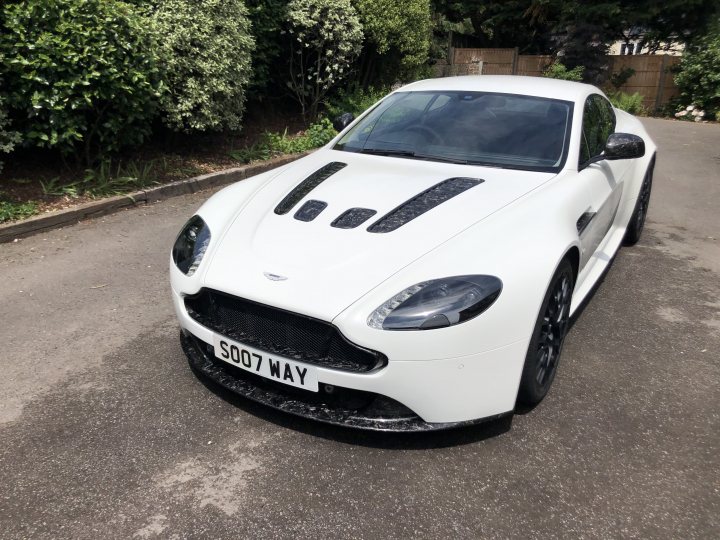 How about an Aston photo thread! - Page 209 - Aston Martin - PistonHeads UK - The image shows a white Aston Martin sports car parked on what appears to be a residential street. The vehicle is sleek and modern, with a distinctive black roof that adds a sporty touch to its overall design. The car is positioned diagonally in the frame, slightly off-center from the camera's perspective. In the background, there's a glimpse of a green lawn and a fence, suggesting a suburban setting. There are no visible people or other vehicles in the vicinity, indicating a quiet neighborhood during the daytime.