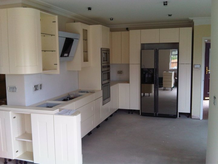 Kitchens Pistonheads - The image displays an interior view of an unfinished kitchen. The kitchen is predominantly white, with various wood elements and paneling. It is designed with a combination of countertop space and full-height units that offer cupboards and drawers. The space looks modern and well-appointed, suggesting a contemporary design. No external windows are visible, and the room itself is bare, without any furniture or personal items, which supports the impression the space is either under construction or not yet in use.