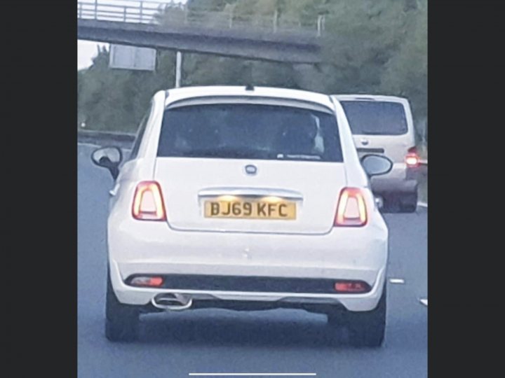 Incongruous Number Plates - Page 1 - Aston Martin - PistonHeads - The image shows a white car on a road. The car appears to be a small hatchback with a visible license plate that reads "B61KH". There is a person sitting in the driver's seat, but their face and details are not clearly visible. In the background, there is another vehicle behind the white car, suggesting traffic flow. The image has a watermark or overlay text that includes the number "29" and what seems to be a username or handle, indicating it may have been taken from a social media platform or is part of a video still.