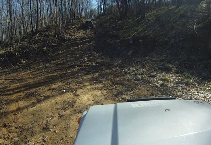 Bit of off-roading, and a bit of camping. - Page 1 - Off Road - PistonHeads - The image displays a rugged, dirt-covered trail with sparse vegetation. In the foreground, a section of a vehicle, specifically suggesting an SUV or similar type of vehicle, is visible. The vehicle appears to be in motion along the dirt road or path. In the background, you can see a line of trees and a dirt hill to the right. The environment suggests this could be a rural or forested area.