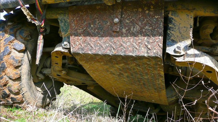 Home made underbody protection - Page 1 - Off Road - PistonHeads - The image shows a close-up view of a massive back tire of a bulldozer that has been ravaged by the elements. The word of a Roman numeral is partially obscured under a muddy tread. There is a tight shot of the wheel, focusing on its textured road-tyres and gears. The damaged and dusty state of the machinery suggests it's been out in the elements for quite some time. This scene provides a stark contrast to what is typically an image of a vibrant construction site.