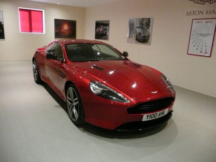 So what have you done with your Aston today? - Page 48 - Aston Martin - PistonHeads - This image features a red Aston Martin car, prominently displayed in a spacious room. The car is positioned so that it occupies the majority of the space in the frame. The lighting in the room highlights the sleek surface of the car, with its reflective nature adding a touch of glamour to the scene.

The background reveals a large opening, suggesting that the room might be part of a showroom or garage concept. A few artworks are hanging on the walls around the car, adding an aesthetic touch to the environment.

On one of the walls, there's a plaque with a design that appears to be related to the brand of the car. The overall setting appears to be well-maintained, with a focus on displaying the car in an elegant and sophisticated manner. The Aston Martin logo is clearly visible on the car, further emphasizing the brand's exclusive association with this vehicle.