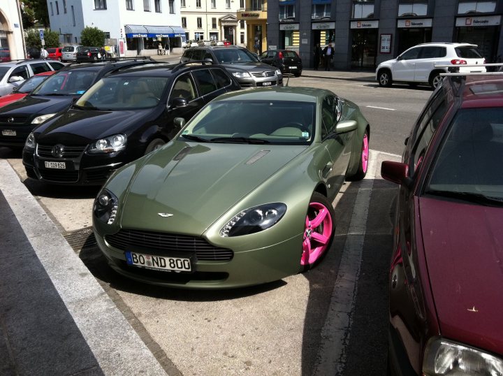 Pistonheads - The image captures a city street scene. A vibrant green sports car with pink rims is the centerpiece, parked near a curb. The car exudes a sense of luxury and speed. Surrounding the green sports car, there are other vehicles parked on the side of the street. Some are black, others are white. The street itself is lined with buildings, and there's a sidewalk for pedestrians. This scene paints a picture of everyday urban life.