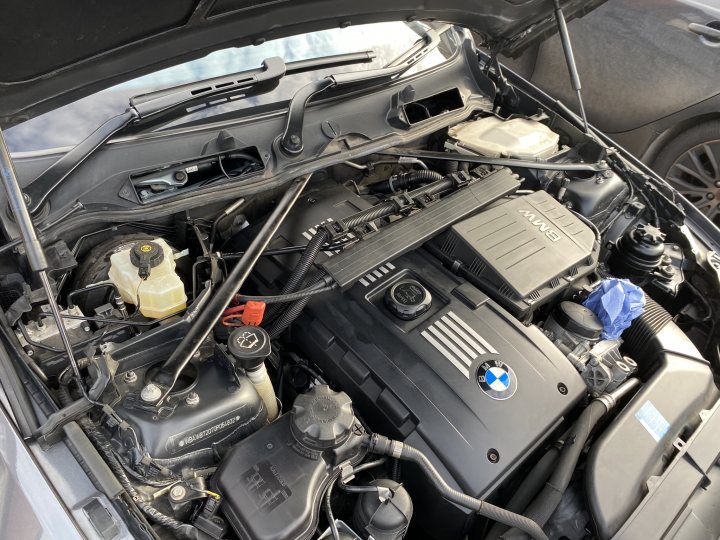 My brave pill; E92 BMW 335i with the infamous N54 engine - Page 43 - Readers' Cars - PistonHeads UK - The image shows the engine bay of a car, which is open and reveals the engine components. A variety of hoses and wires are visible, along with the engine itself. At the top of the image, a black object is hanging down, possibly part of a lifting mechanism or an accessory for vehicle maintenance. There are no people present in the image. The car appears to be stationary, as there are no indications of movement or operation.