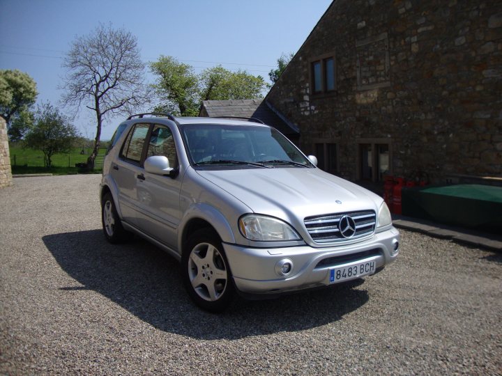 Show us your Mercedes! - Page 9 - Mercedes - PistonHeads - The image features a sleek silver Mercedes-Benz car parked on a gravel driveway. The vehicle, positioned prominently in the foreground, sports a modern design with chrome accents, including grille and headlight trim. Behind the car, a sturdy stone building with traditional features serves as the backdrop. In the background, a glimpse of a lush green tree can be seen, adding a touch of nature to the scene. The image exudes a contemporary yet rustic charm, with the car's polished appearance contrasting nicely with the rugged textures of the stone house and gravel driveway.