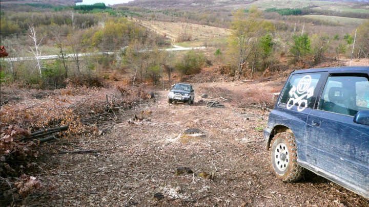 Couple of pics from today... - Page 1 - Off Road - PistonHeads - The image presents a rugged off-road scene. Dominating the foreground is a blue SUV, its body heavily covered in mud and dirt. The vehicle is partially obscured by a pile of logs, hinting at a momentary pause in the journey. 

A couple of obstacles lie in the middle of the road; a car and a small dumpster are visible, both partially covered by fallen tree branches. 

The road itself is not paved, a trail tracing its path through the wilderness. It cuts through a dense cover of trees, their brown and green hues suggesting a late autumn or winter setting. 

The field at the sides of the road is populated with a smattering of rocks and scattered trees, adding to the sense of a remote, untamed landscape.