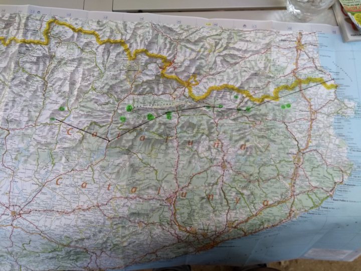 Crossing the Pyrenees East to West - Page 1 - Off Road - PistonHeads UK - The image shows a large map spread out on a table. On the map, there's a yellow line that seems to mark a route or trail across the region it covers. The map features roads and paths, indicating a network of transportation in the area. There are also various symbols and markings on the map, suggesting it could be used for navigation or planning purposes. The setting appears to be indoors, as indicated by the presence of what looks like a whiteboard with writing on it, visible behind the map.