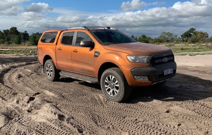 Cooper AT3 4S good on ranger wildtrack - 265/65r18? - Page 1 - Off Road - PistonHeads - The image shows a vibrant orange SUV, a Ford Ranger model, parked on a muddy area with deep tire tracks around it. The vehicle is captured in daylight and appears to be in motion or has just stopped, as indicated by the tire marks. There are no visible texts or distinctive markings that indicate branding or any other specific information. The background is quite nondescript with open land, a field, and some indistinct foliage. This could suggest a rural or semi-rural setting, possibly for off-road activities given the vehicle's condition and location.