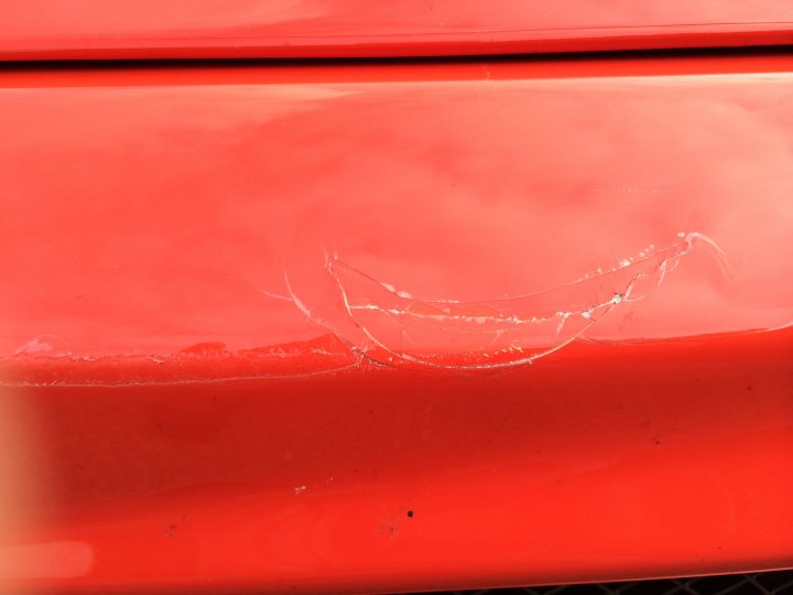 Kudos for guessing which classic supercar's.... - Page 1 - Ferrari V8 - PistonHeads - The image showcases a red car with a visible crack or chip on the hood. The damage to the car is located on the left side. It appears to be quite thin in places, with the impact causing a raised line. The paint around the damage is glossy and smooth, contrasting with the rough texture of the cracked area. The overall appearance suggests recent dental work on the hood.