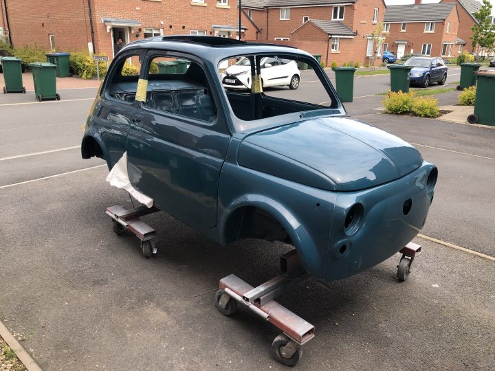 The fiat 500 nobody wanted to save - Page 2 - Classic Cars and Yesterday's Heroes - PistonHeads UK - The image shows a classic blue Fiat 500 car parked on a street. The vehicle is characterized by its round headlights and compact size, typical of older Fiat models. It appears to be in the process of restoration or modification, as indicated by the visible bodywork and missing parts such as doors and hood. The car is elevated on jack stands, which are commonly used for automotive repairs or customization work. The surrounding environment includes a residential area with houses and a driveway, suggesting that the photo was taken in a suburban neighborhood.