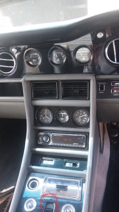 Have we been foolish? Yes but we're all grinning from ear to - Page 1 - Rolls Royce & Bentley - PistonHeads - The image showcases the central console area of a luxury car. It features several dials indicating controls for various systems such as air conditioning and electrical windows. The dials vary in size and position, some are larger with other smaller ones. A prominent X-shaped dial takes up a significant portion of the console. The console is made of a silver-colored metal extending into a glove compartment. The material has a reflective surface, adding to the elegant look of the vehicle's interior.