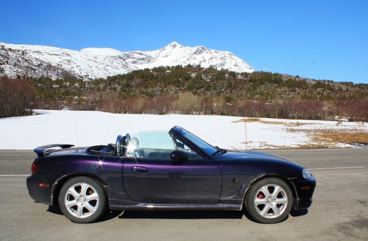 Respraying the Mk1 - what colour? - Page 1 - Mazda MX5/Eunos/Miata - PistonHeads - The image shows a vibrant purple sports car parked on a street with a clear view of a snowy mountain in the background. There are three visible tires on the car, it appears to be a convertible with the top up. The sky above is a brilliant blue and the overall setting suggests a colder, possibly mountainous, region. The car's shiny exterior gleams against the snowy landscape, creating a striking contrast.