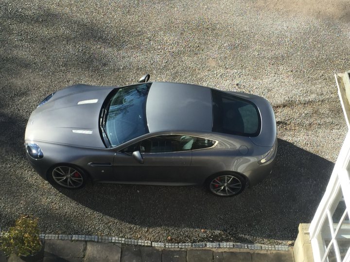 So what have you done with your Aston today? - Page 252 - Aston Martin - PistonHeads - This image showcases a sleek, gray Aston Martin sports car parked on a gravel driveway. The car, which is the only object in the picture, features a sloping roofline and large windows, giving it a dynamic and modern appearance. The vehicle's design and details, such as the distinctive grille and the aerodynamic lines, are clearly visible. The background of the image reveals a clear sky above and not much else surrounding the parked car, putting the focus entirely on the Aston Martin.