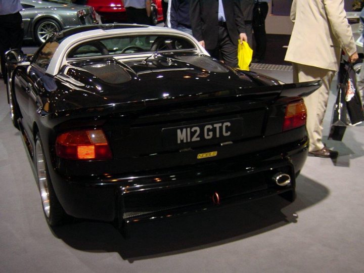 A car that is sitting in the grass - Pistonheads - In the image, an elegant sports car is the center of attention. The car is black and silver, parked inside a building, and has a tail number of M12 GTC. Behind the car, at a show or an event, there are several people, two of whom are dressed formally in suits. They are observing the car closely, suggesting an interest in the vehicle. The overall atmosphere appears to be a social or industrial event, possibly related to automotive history or luxury.