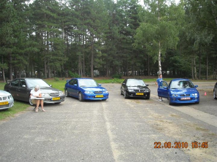 Pistonheads - In the image, there is a parking lot surrounded by greenery where a group of cars are parked in a diagonal alignment. Each car is distinctively painted in different colors, which include blue, silver, and shopko's signature orange, creating a vibrant contrast against the natural backdrop. The lot seems deserted except for one person who can be seen sitting alone on the left side of the image. In the bottom right corner of the image, the date and time are subtly marked, signaling the exact moment this scene was captured.