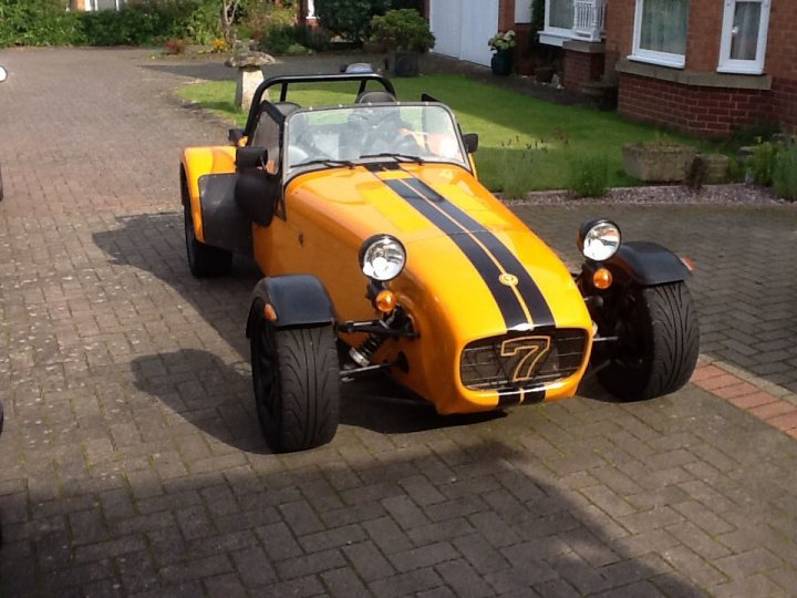 A red motorcycle is parked in a parking lot - Pistonheads - The image features a striking two-door yellow sports car with a convertible soft top roof, parked on a brick driveway. The car's color and design suggest speed and style. The convertible top is in the up position, indicating the sunny weather. The car is nearby to a house, as suggested by house plants and its close proximity to the residential structure's facade. The surrounding area appears to be a quiet, residential setting.