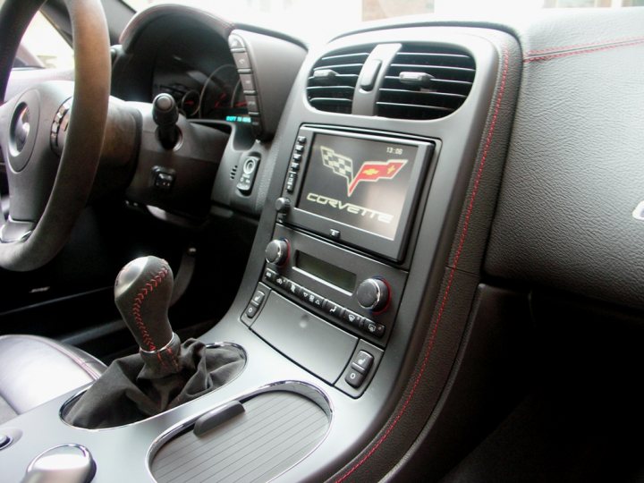 Corvette Z06 Centennial Edition for sale in the UK - Page 1 - Corvettes - PistonHeads - This is an interior view of a vehicle's cockpit, specifically focusing on the passenger side. The dashboard is in a racecar-like design, with a Corvette logo prominently displayed in the center console. The gear shifter is made of wood, and there are additional controls on the center console suggesting the vehicle is equipped with advanced features. The steering wheel and passenger side mirror are visible, providing a complete picture of the driver's area.