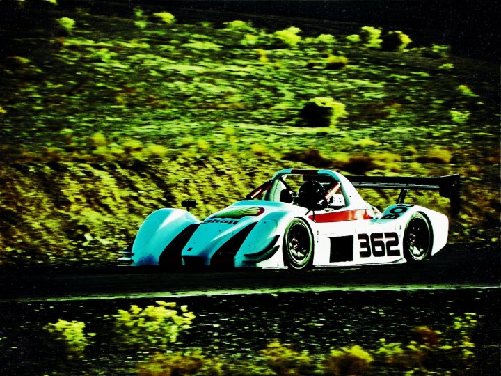 It's Good To Be King - Page 1 - Radical - PistonHeads - The image captures a dramatic scene on a black and gravel track. Dominating the scene is a vibrant blue and white race car, labeled with the number "362". This isn't just any vehicle - it has a large rear wing, suggesting it's a high-performance road car derived from the manufacturer's motorsport activities. The car is piloted by a driver, focused on the winding track ahead. The backdrop is a lush, wild landscape, with dense greenery adding a sense of drama and competition to the scene.