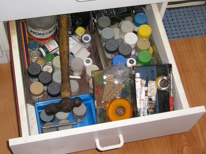 Box Tool Pistonheads Modelling - The image captures the top drawer of a desk, filled with a variety of items. A brown drawer separator provides organization within the drawer. An assortment of cylindrical objects, possibly paint chips or shop tools, occupies one part of the drawer. Adjacent to them, a roll of yellow masking tape suggests some form of DIY project or past hobby. Other objects include several open glass jars and a black-handled scissors, which could be used for office or arts and crafts purposes. An open blue drawer beneath catches a glimpse of some tools. The drawer is visibly full, indicating an active and task-filled workspace.