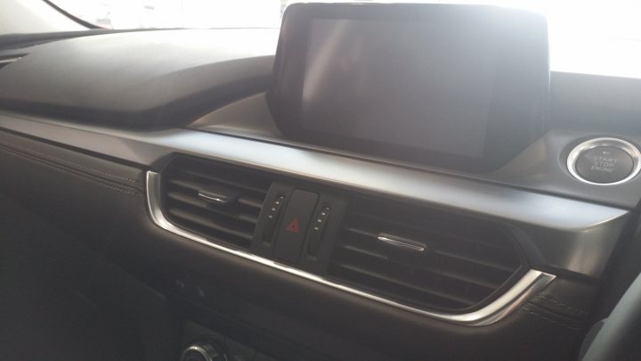 A black and white photo of a black and white car - Pistonheads - The image features the dashboard of a modern car. The central focus is a large screen display that is integrated into the dashboard. The screen seems to be off, giving the impression of a blank television screen. Below the screen, there are multiple controls and buttons, which are likely associated with the car's media and navigation system. The dashboard itself is sleek and shiny, with a reflective surface that adds to the refined aesthetics of the car's interior. It appears to be taken from the passenger's side, offering a clear view of the driver's side panel with the controls.