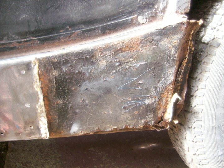 Pistonheads - The image shows a close-up view of a vehicle's bumper, which appears to be predominantly metallic with a darkish-brown color. The paint on the bumper is peeling off in several places, exposing the underlying metal. There are signs of rust in some areas, especially along the joints and edges where the metal is connected or clamped to other parts of the vehicle. The texture of the metal shows indentations, likely from the stainless steel mesh that is used to reinforce the bumper. The bumper is connected to the plastic wheel arch in the foreground, indicating it is part of the vehicle's off-road bumper assembly.