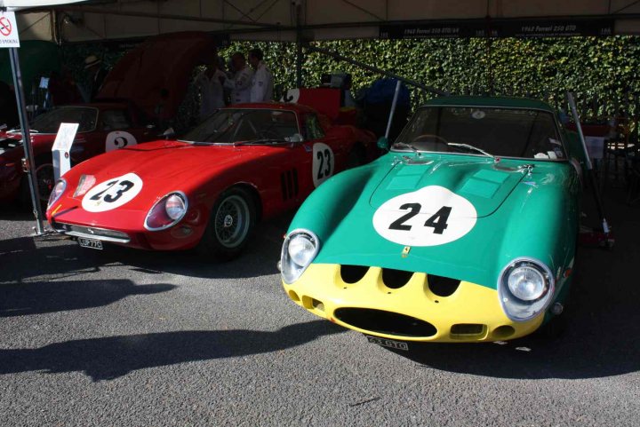 Revival images - Friday  - Page 1 - Goodwood Events - PistonHeads - The image captures a scene on a street where three vintage cars are on display. Two of the cars are painted in sleek, glossy red, and the third one is a vibrant green and black. Each car bears the number 24, and they all sit side by side, as if ready to roar into life. The backdrop is a simple blue wall, providing a stark contrast to the colorful cars. The street where they're parked is lined with buildings, and a few people can be spotted in the distance, perhaps admiring the retro beauty of these vehicles.