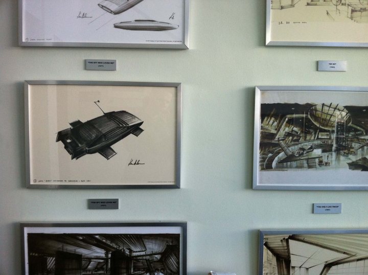 Pinewood Pistonheads Studios - This image showcases a collection of artwork, possibly drawings or sketches, prominently displayed on the wall in a museum or gallery setting. Each piece is individually framed and accompanied by a plaque, indicating their titles and possibly the artist's name or a brief description. The style of drawing varies across the pieces, suggesting a range of creative expressions. Some pieces depict futuristic structures, while others, such as the monochromatic one on the top left, seem more abstract or abstract in nature. The artwork seems to be associated with online design and exploration, perhaps representing early digital or digital manipulation art methods, which might be a unique focus for this particular exhibit.