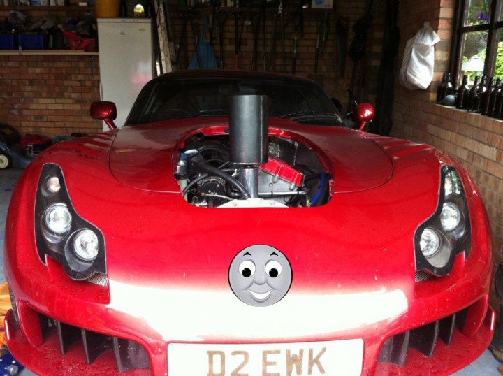 Cooling System Purge and Refill Tool - Page 1 - Speed Six Engine - PistonHeads - The image shows a parked red sports car with an emblem displayed on the front grille featuring a moon face. The car has its hood propped open, revealing its engine and associated components. The car's license plate reads "D2 EWK". In the background, there is a cluttered storage area with various items scattered around.