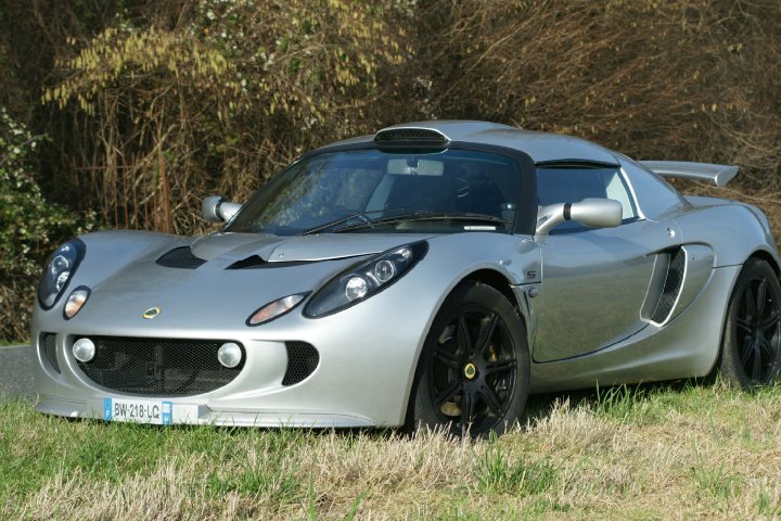 Why not sold? - Page 1 - Elise/Exige/Europa/340R - PistonHeads - This image showcases a silver sports car parked on the side of a road. The car is positioned at an angle to the viewer, allowing for a clear view of its sleek design and smooth paintwork. It features a prominent spoiler on the rear deck and a large air intake at the front. Enhancing the sporty look are a set of black rims paired with a low ground clearance. The car is situated in a natural setting with vegetation around, suggesting this scene might be set in a less urban environment.