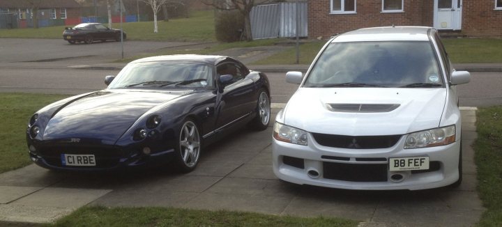 Best 2 Car Combos - Page 7 - General Gassing - PistonHeads - The image shows two sports cars parked side by side on a concrete driveway. The car on the left is a dark blue color and appears to be a more aggressive, possibly a European sports car. The car on the right is white, with a noticeable rear spoiler and a different, more contemporary design, and it has a UK-style license plate on the front. Both cars have a low and wide stance, which is a common feature in sports cars. In the background, there's a residential area with houses and a clear sky, indicating the photo may have been taken during the day under good weather conditions.