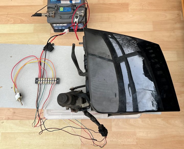 Mazda MX-5e Tesla Powered - Page 9 - Readers' Cars - PistonHeads UK - The image depicts a home setup with various electronic devices. A television is placed on the floor, connected to an open laptop by cables. There's a device that appears to be an automatic projector with its screen up and displaying something that isn't clear in the photo. The projector is hooked into the laptop via additional wires. To the side, there are other electronic devices, including what seems to be a drone controller or a radio-controlled car, which also has cables attached to it. The setting suggests a hobbyist or electronics enthusiast's workspace where different devices and accessories are used for entertainment, education, or work purposes.