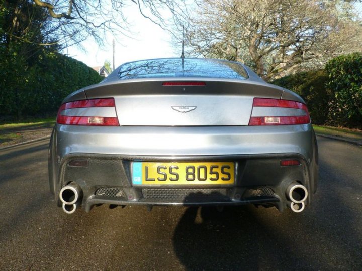 Badly modified cars thread Mk3 - Page 118 - General Gassing - PistonHeads UK - The image displays a silver sports car parked on a paved surface, likely a driveway. The car is positioned at an angle that allows for the view of its rear and part of its side profile. It features a visible exhaust system with two pipes on each side, typical of high-performance cars. There's a license plate at the back indicating the car has been registered in the United Kingdom, specifically in Leicestershire. The vehicle is positioned behind a small, green hedge that adds a touch of color to the scene.