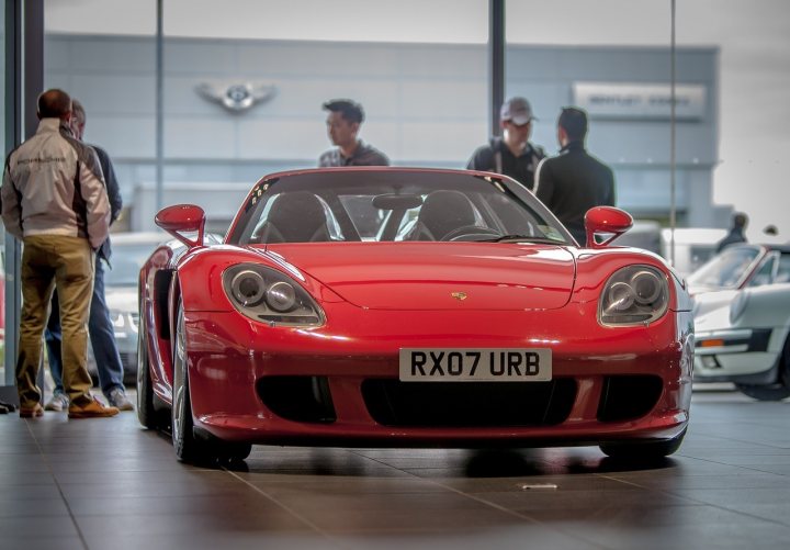 The Best ///M/Barge/General Rant/Look at this/O/T (Vol XVI) - Page 422 - General Gassing - PistonHeads - The image features a shiny red sports car parked indoors, possibly in a showroom. There are several other vehicles visible in the background. Three men stand beside the sports car, looking at it with interest. They are dressed casually, suggesting they might be potential buyers or curious spectators. The car's polished finish reflects the overhead lighting, enhancing its visual appeal.