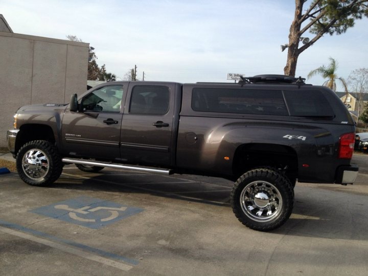 If you could, would you? - Page 1 - Yank Motors - PistonHeads - The image features a large, gray metallic truck parked outdoors in a parking lot. The truck is large and appears to be an SUV or pickup truck due to its size and design. It has five doors and four wheels, suggesting a crew cab version catering to larger groups or families. The truck is designed with a full-size spare tire mounted on its roof, and it also prominently displays an "8-Sided Candy" for sale sign in the window, indicating that it might be a mobile food stand or used for personal measures. The vehicle is parked beside a tall tree and is situated on asphalt, with blue stripes visible marking a specific section or lane of the parking lot.