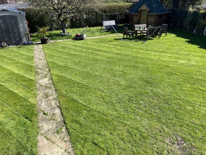 2023 Lawn Thread - Page 14 - Homes, Gardens and DIY - PistonHeads UK - The image shows a well-maintained backyard with a neatly trimmed lawn. There's a wooden deck at one end, surrounded by a patio area. A small shed is also present on the left side of the yard. In the background, there's an apple tree and a fence that marks the boundary of the property. The ground is covered in grass, suggesting it's likely spring or summer. There's no visible text or any specific actions taking place. The overall scene is peaceful and well-kept, indicative of a well-maintained outdoor space.